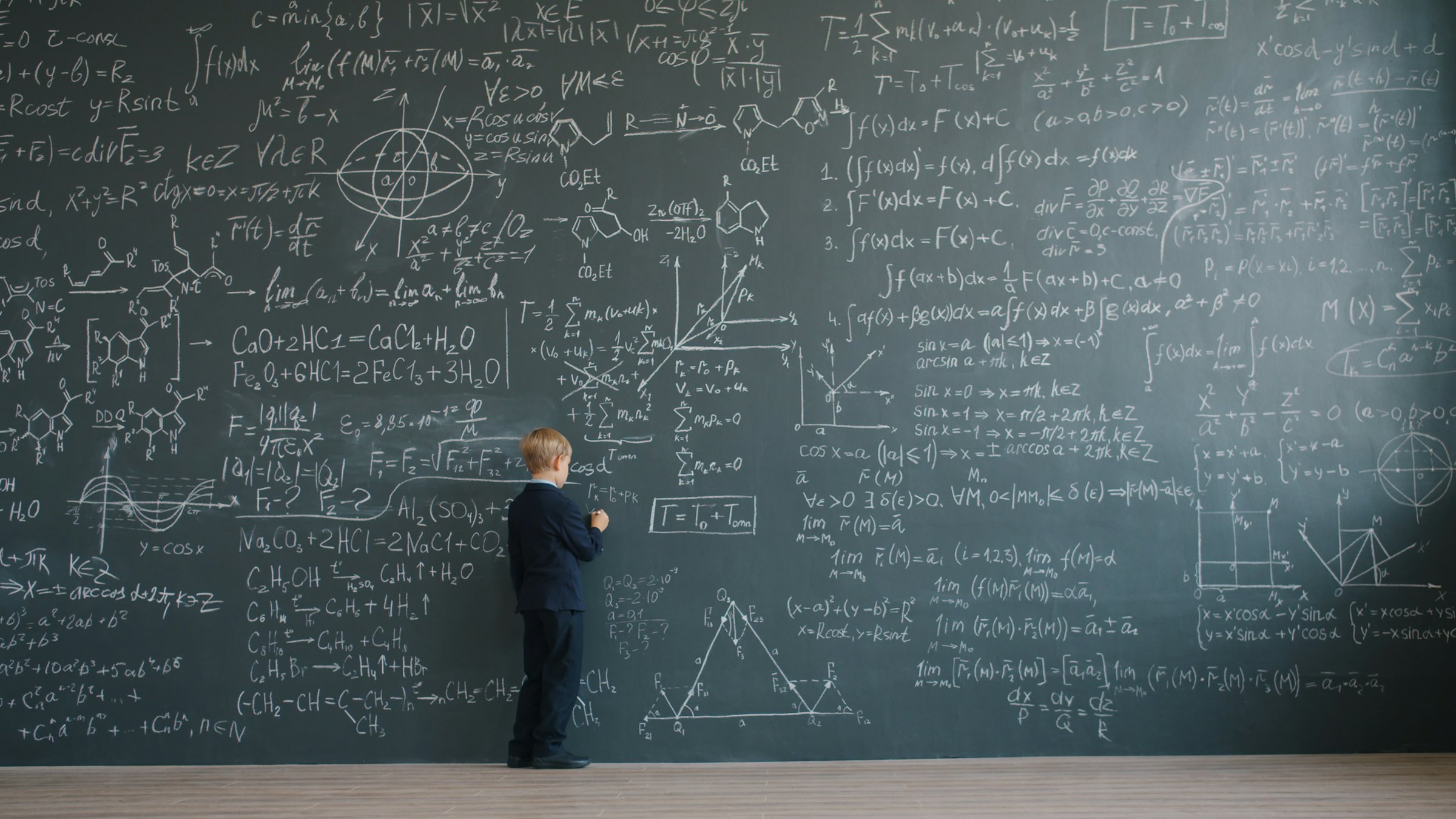 A young student stands before a vast blackboard covered in equations.